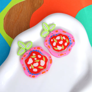 Colorful earrings with a geometric food pizza design on a white dish against a multicolored background